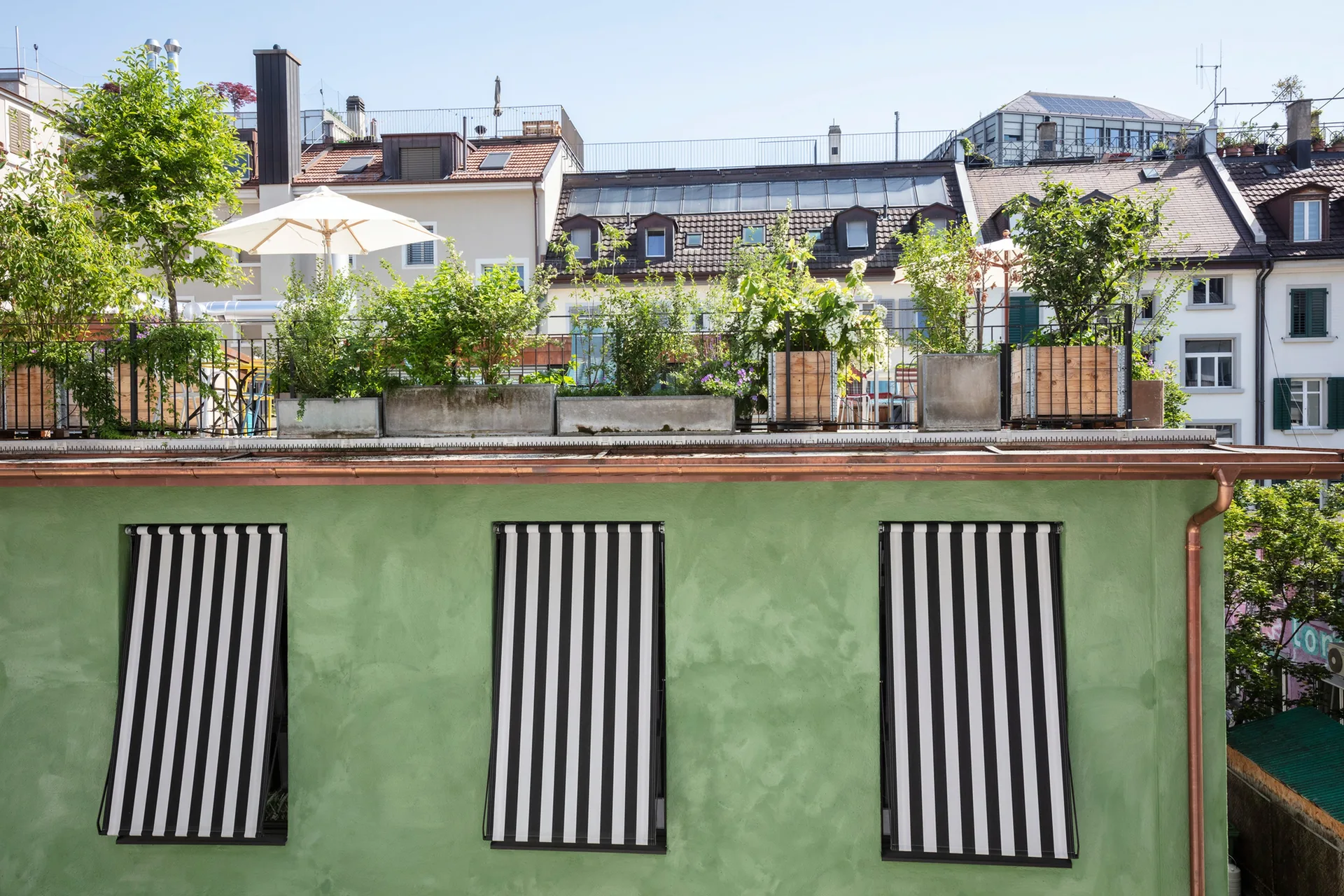 Dachterrasse über der grünen Fassade mit gestreiften Markisen