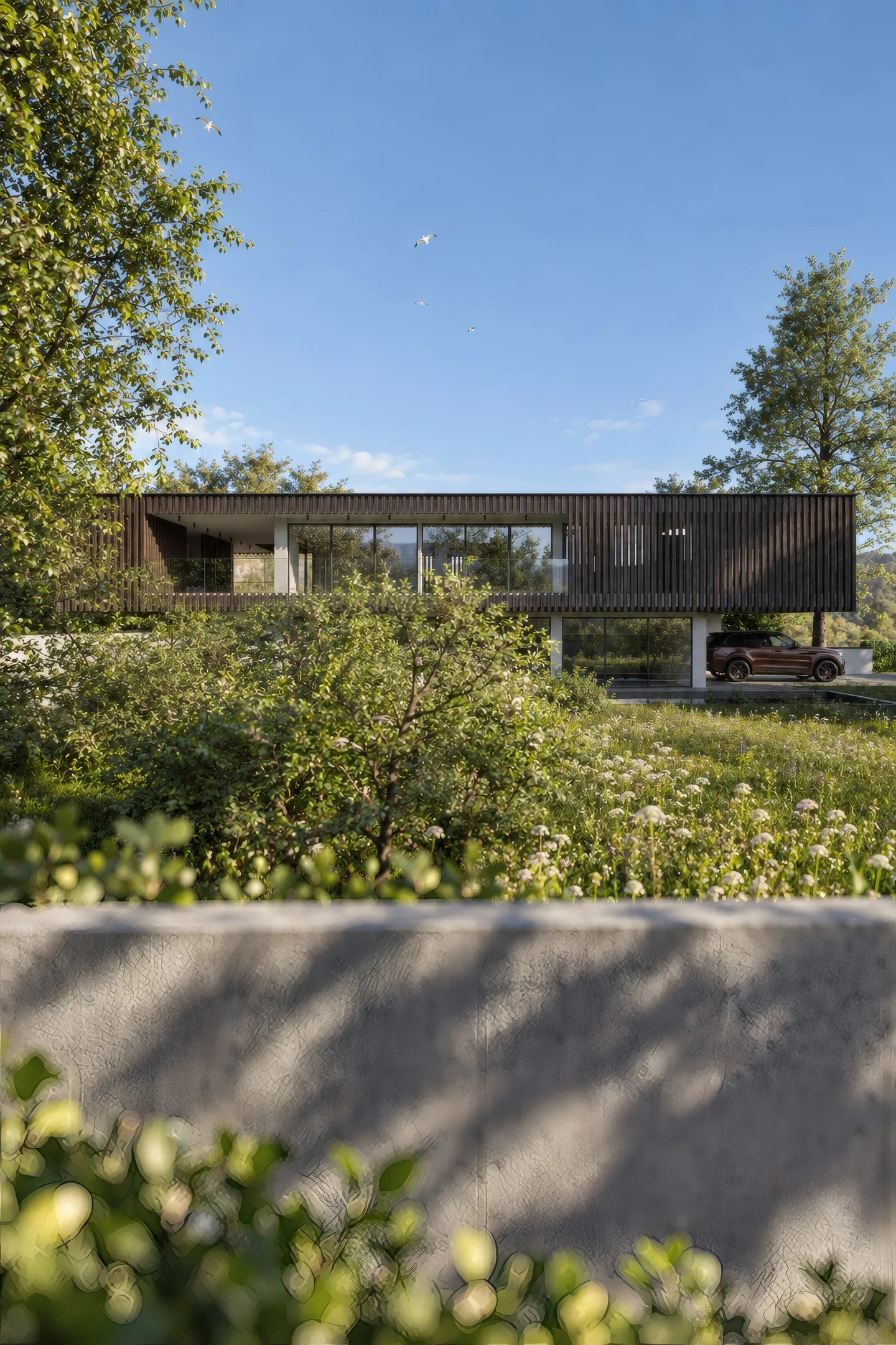 Das Haus von der Wiese aus, hinter einer Betonmauer