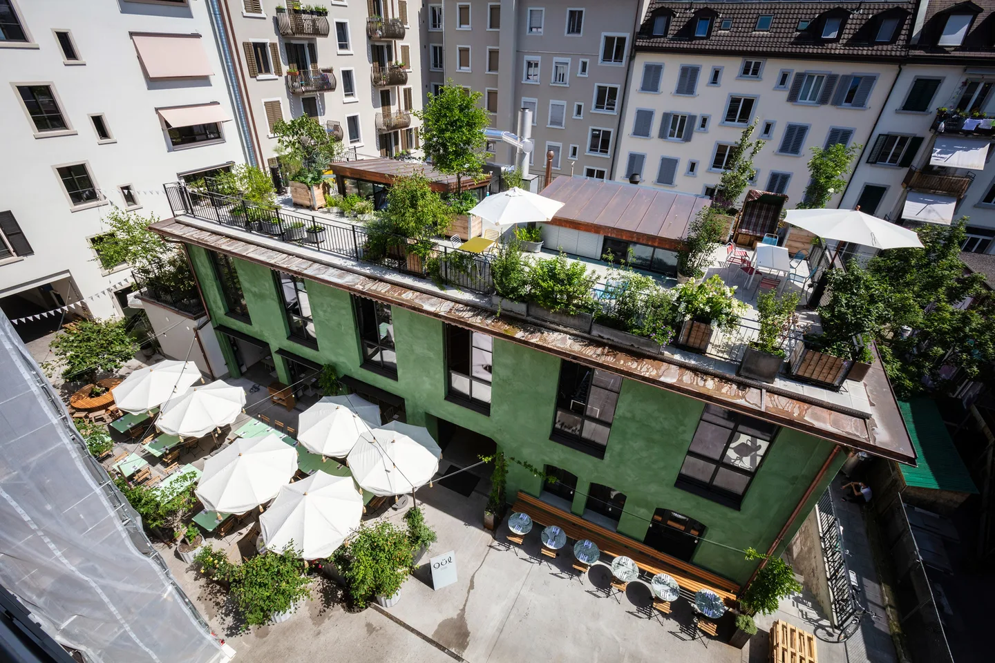 Tellhof – Blick von oben in den Innenhof mit Sonnenschirmen, das grüne Hofgebäude mit begrüntem Dach