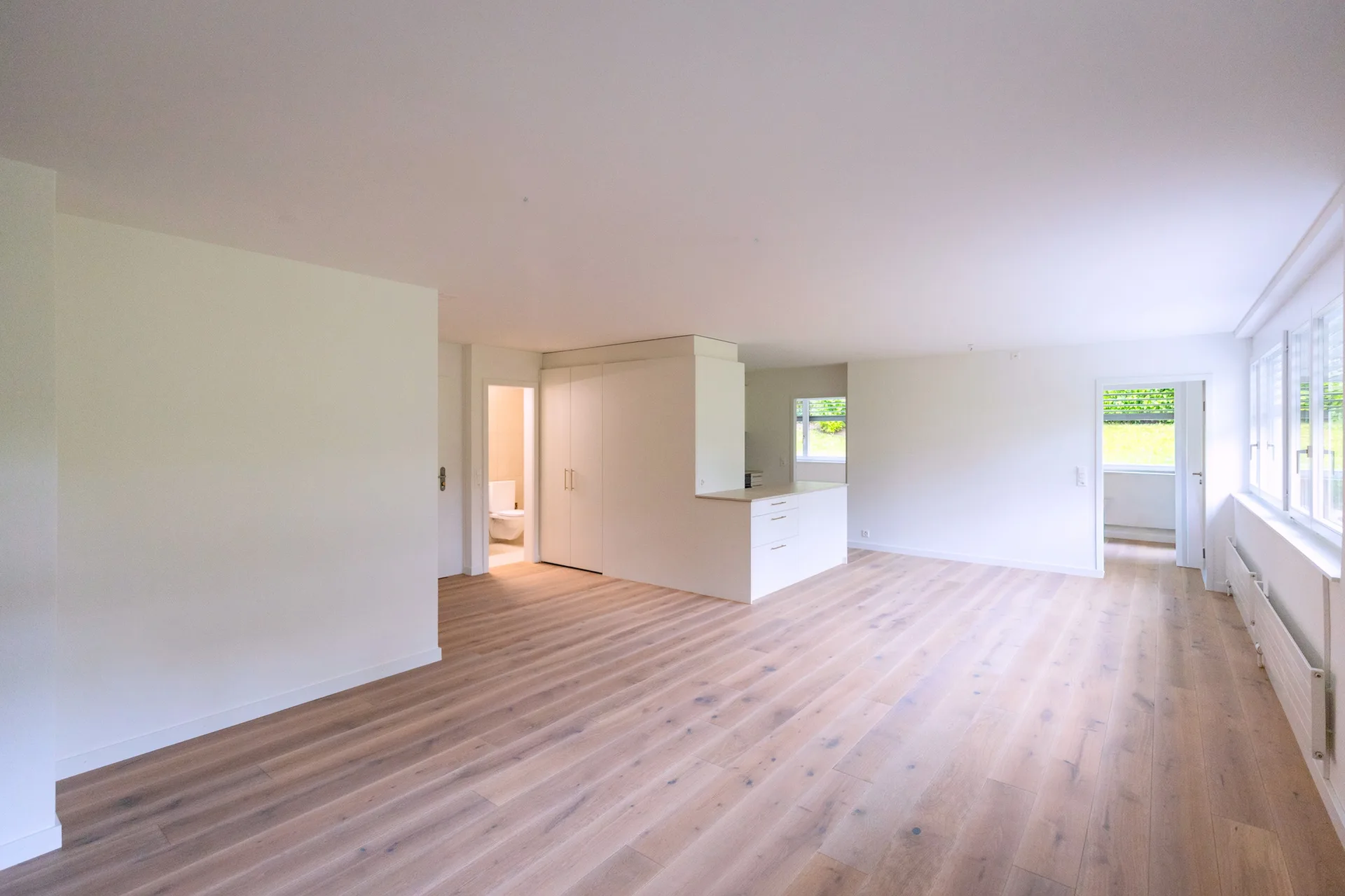Raumübersicht mit Küche, Fensterfront und Eichenparkett